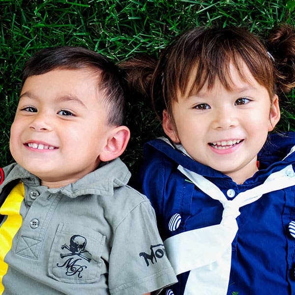 Siblings with dark hair lying on their backs in the grass